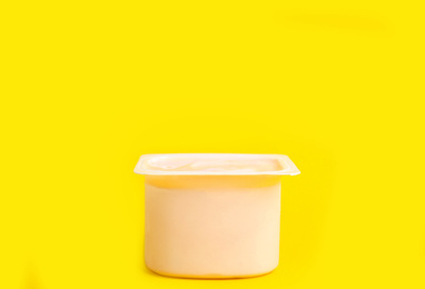 Photo of Tasty organic yogurt in plastic cup on yellow background