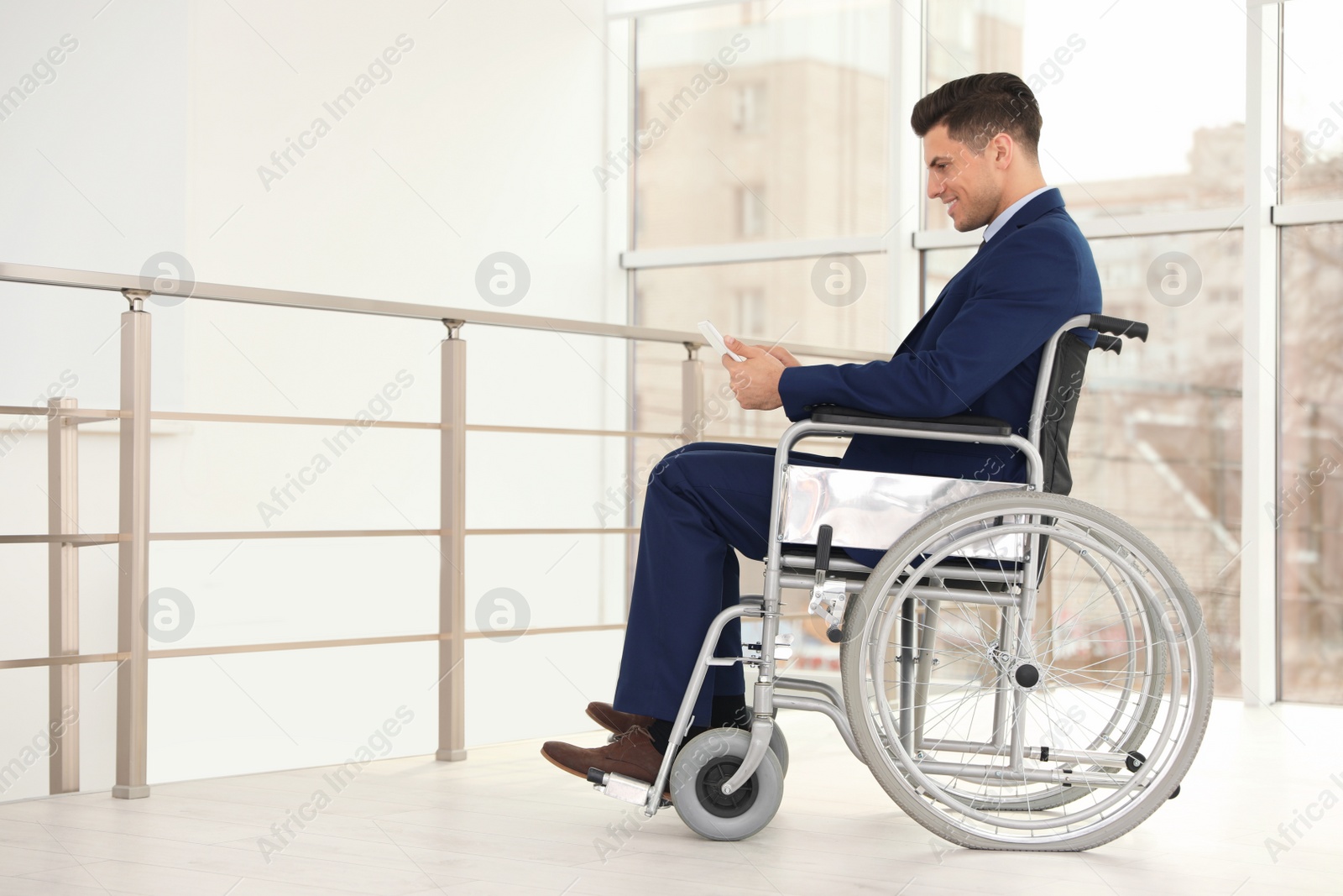 Photo of Young businessman in wheelchair using tablet near window indoors