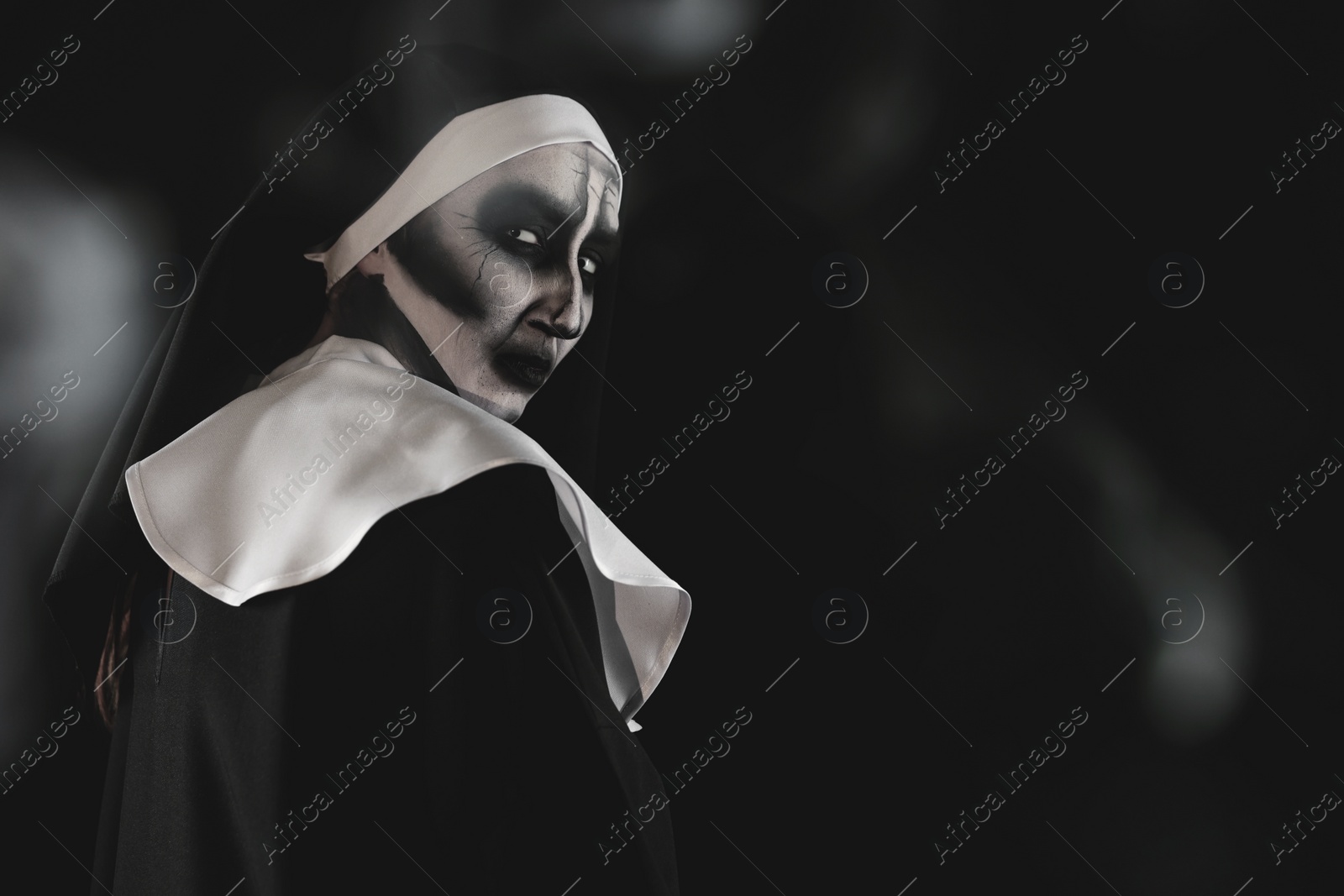 Photo of Portrait of scary devilish nun and smoke on black background, space for text. Halloween party look