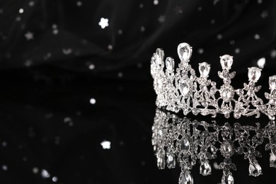 Photo of Beautiful silver tiara with diamonds on dark mirror surface, closeup. Space for text