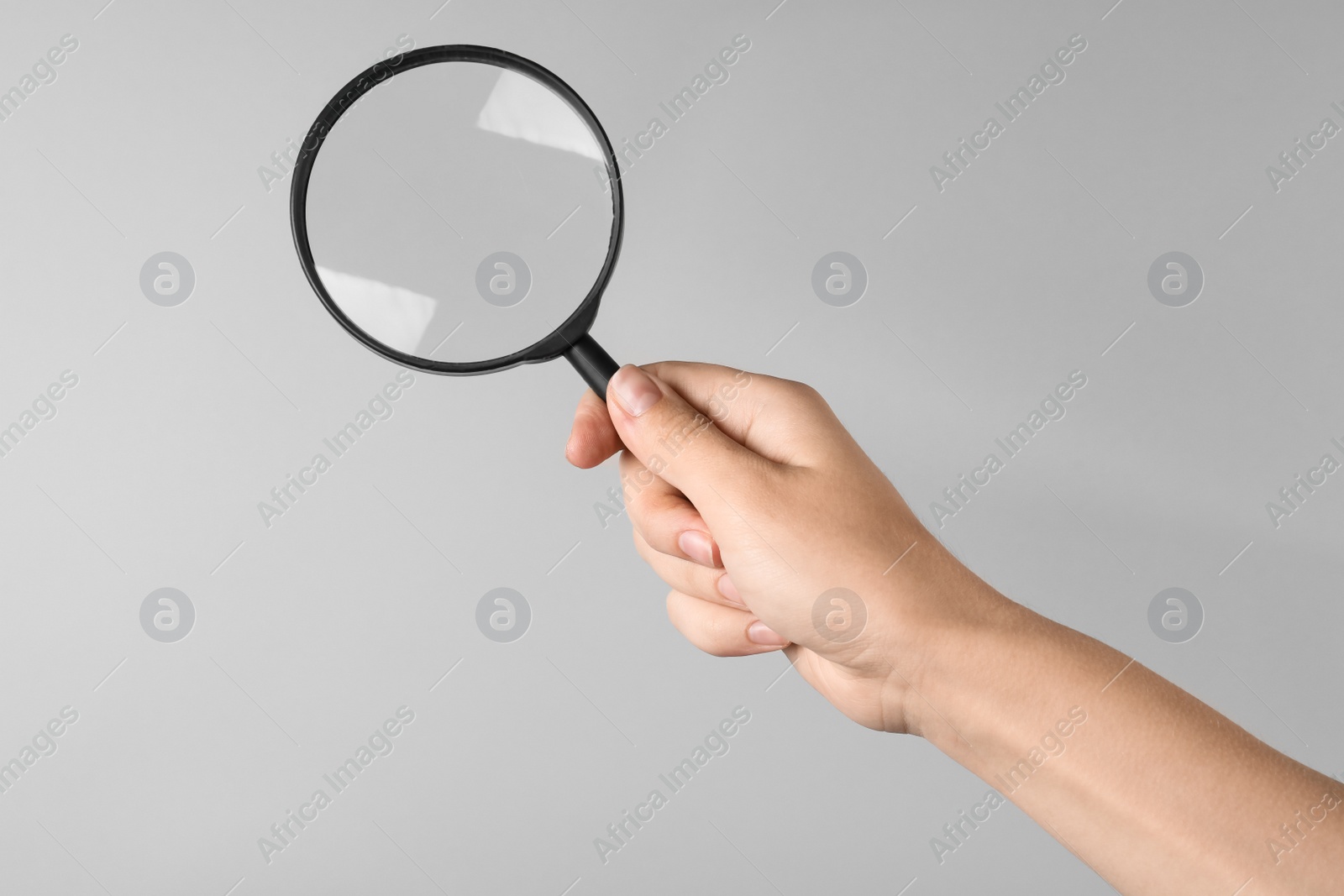 Photo of Woman holding magnifying glass on grey background, closeup. Find keywords concept