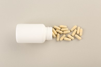 Bottle and vitamin capsules on light background, top view