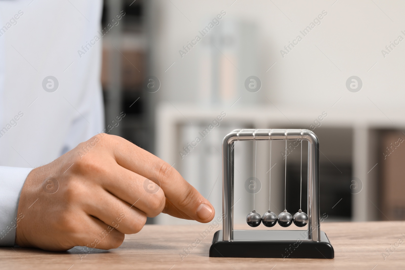 Photo of Man playing with Newton's cradle at table, closeup. Physics law of energy conservation