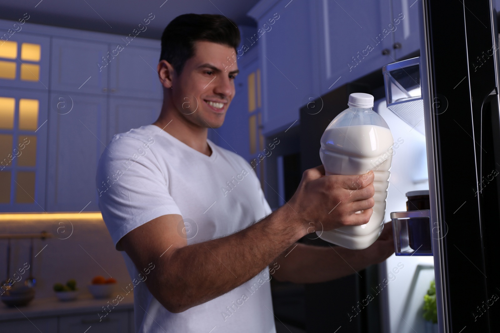 Photo of Man holding gallon bottle of milk near refrigerator in kitchen at night