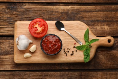 Delicious adjika sauce in bowl and ingredients on wooden table, flat lay