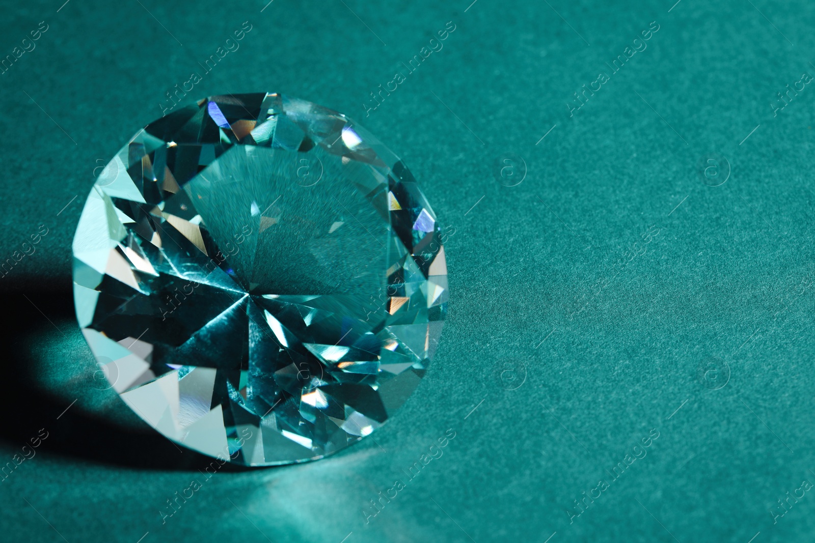 Photo of Beautiful dazzling diamond on green textured background, closeup. Space for text