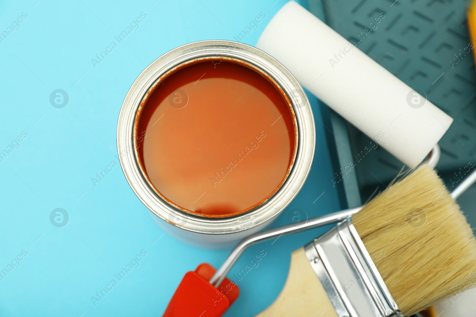 Photo of Can of orange paint, brushes, rollers and container on turquoise background, flat lay