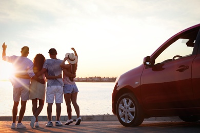 Group of friends near car outdoors at sunset, back view. Summer trip