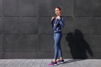 Photo of Beautiful woman in stylish gym clothes near dark grey wall on street, space for text
