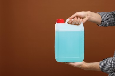 Photo of Man holding canister with blue liquid on brown background, closeup. Space for text