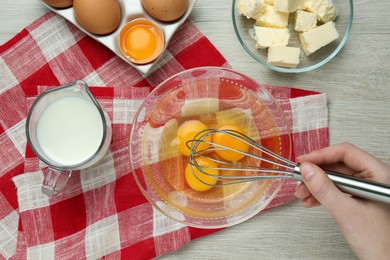 Woman whisking eggs at white wooden table, top view