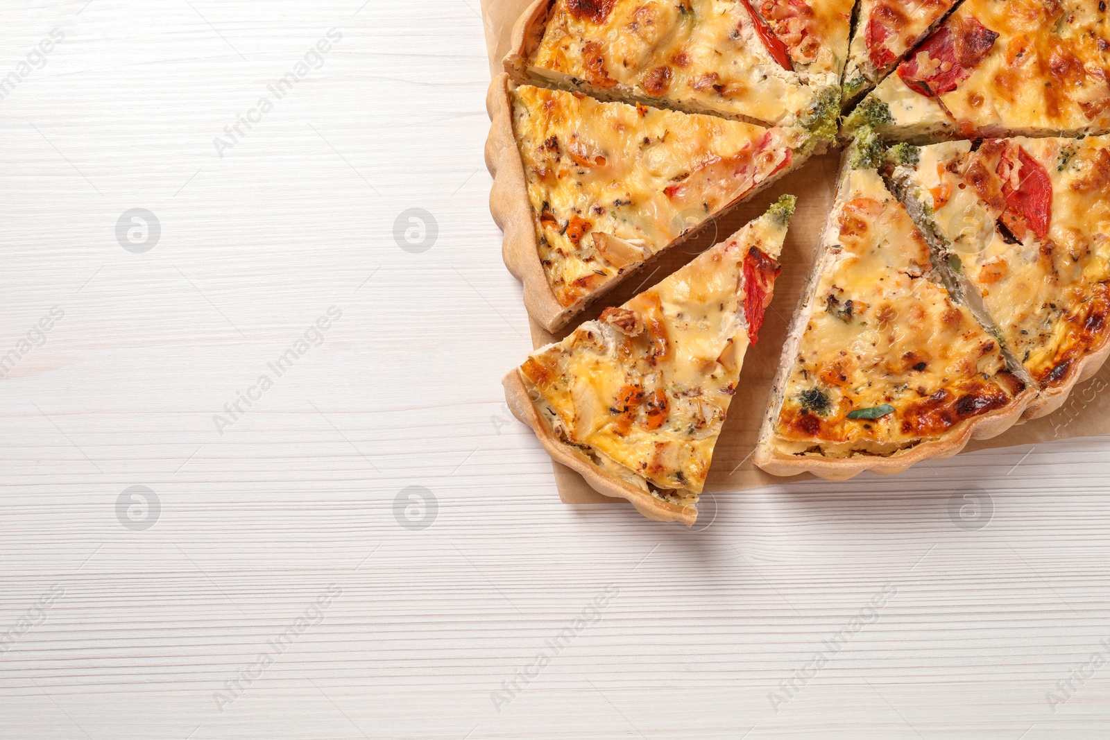 Photo of Tasty quiche with tomatoes and cheese on white wooden table, top view. Space for text