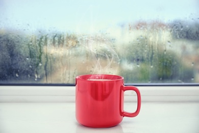 Image of Cup of delicious hot drink on window sill after rain 