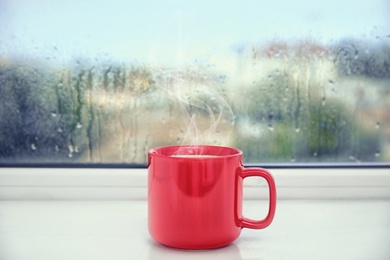 Cup of delicious hot drink on window sill after rain 