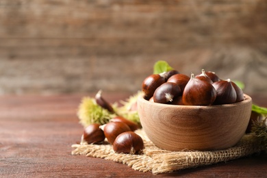 Photo of Fresh sweet edible chestnuts on brown wooden table, closeup. Space for text