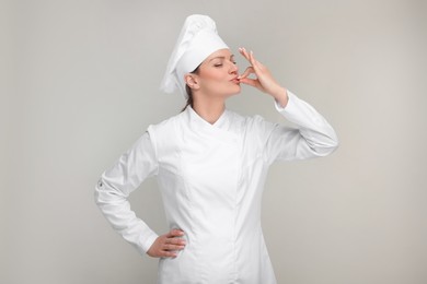 Woman chef in uniform showing perfect sign on grey background