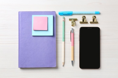 Flat lay composition with smartphone and stationery on white wooden table