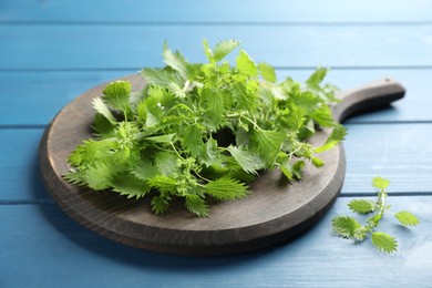 Photo of Board with fresh stinging nettle leaves on blue wooden table