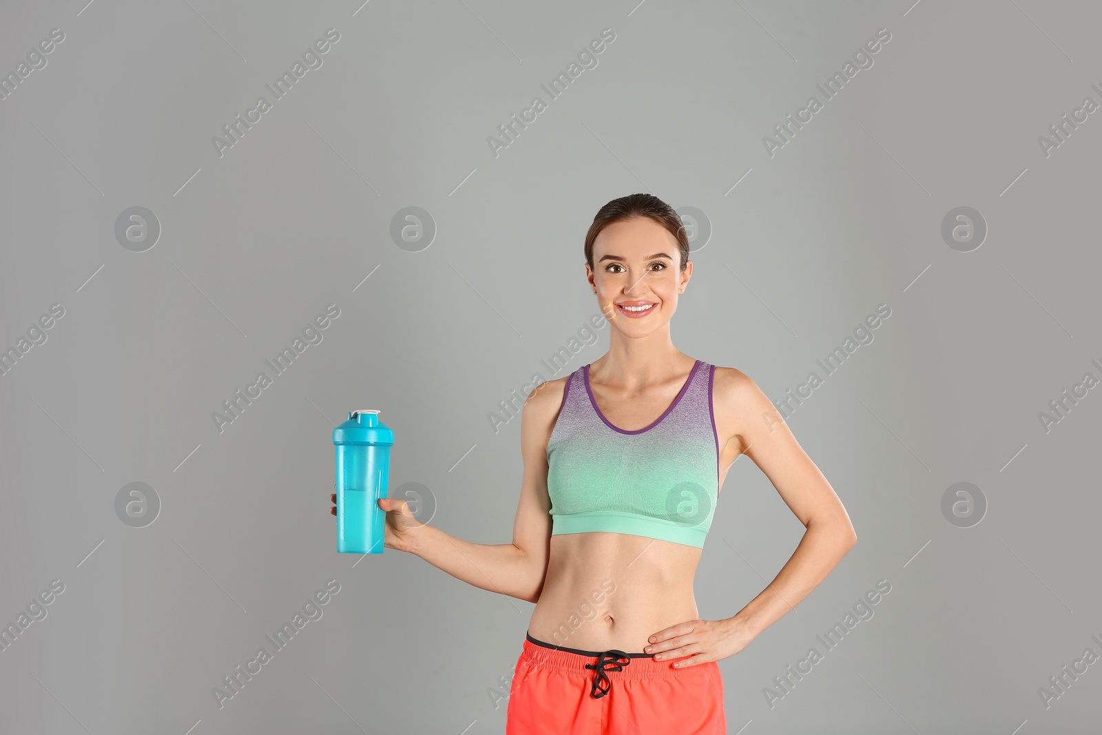 Photo of Athletic young woman with protein shake on light grey background