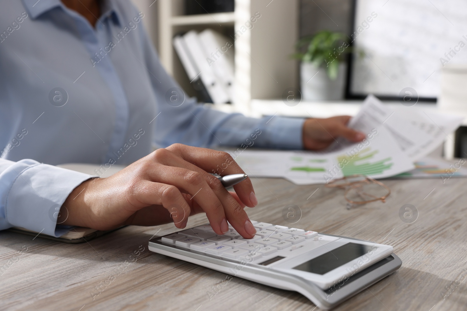 Photo of Woman using calculator at light wooden table in office, closeup