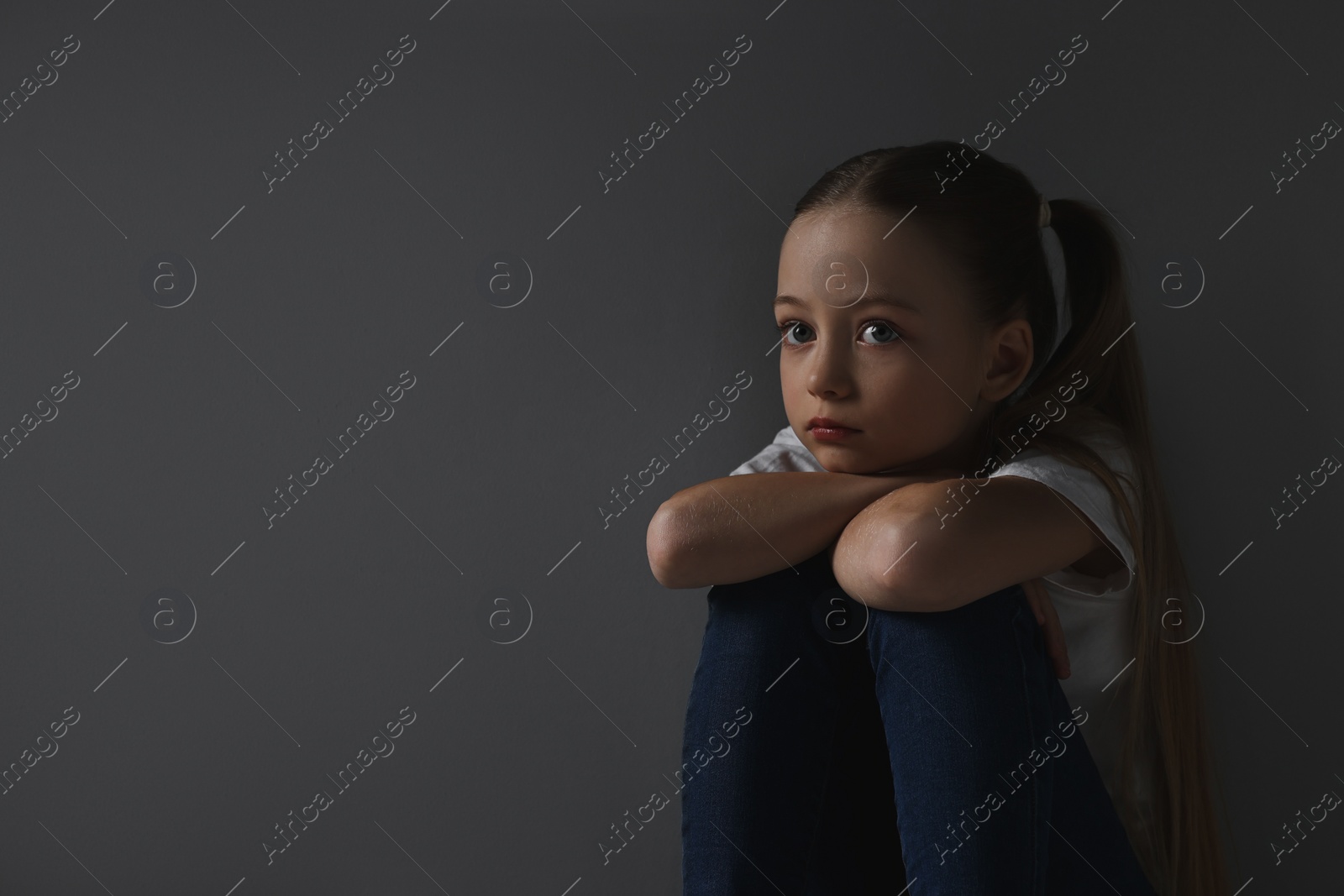 Photo of Sad girl sitting near dark grey background, space for text