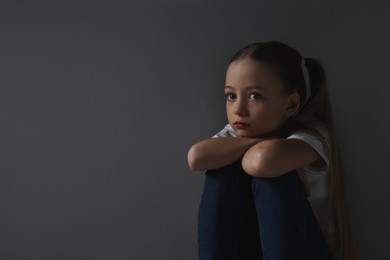 Sad girl sitting near dark grey background, space for text