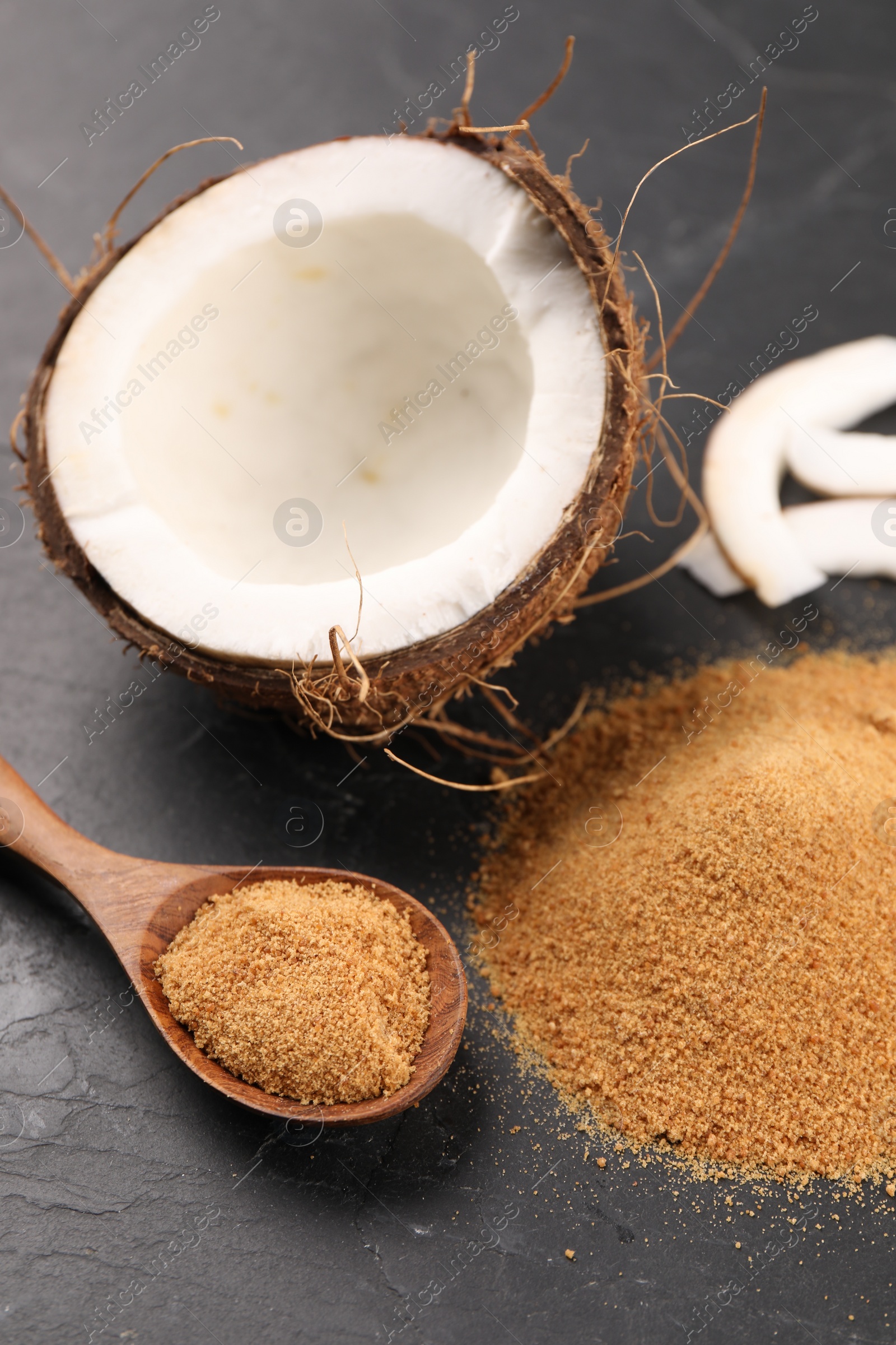 Photo of Coconut sugar, spoon and fruit on dark textured table, closeup