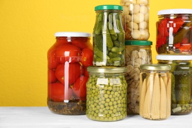 Photo of Jars of pickled vegetables on white wooden table