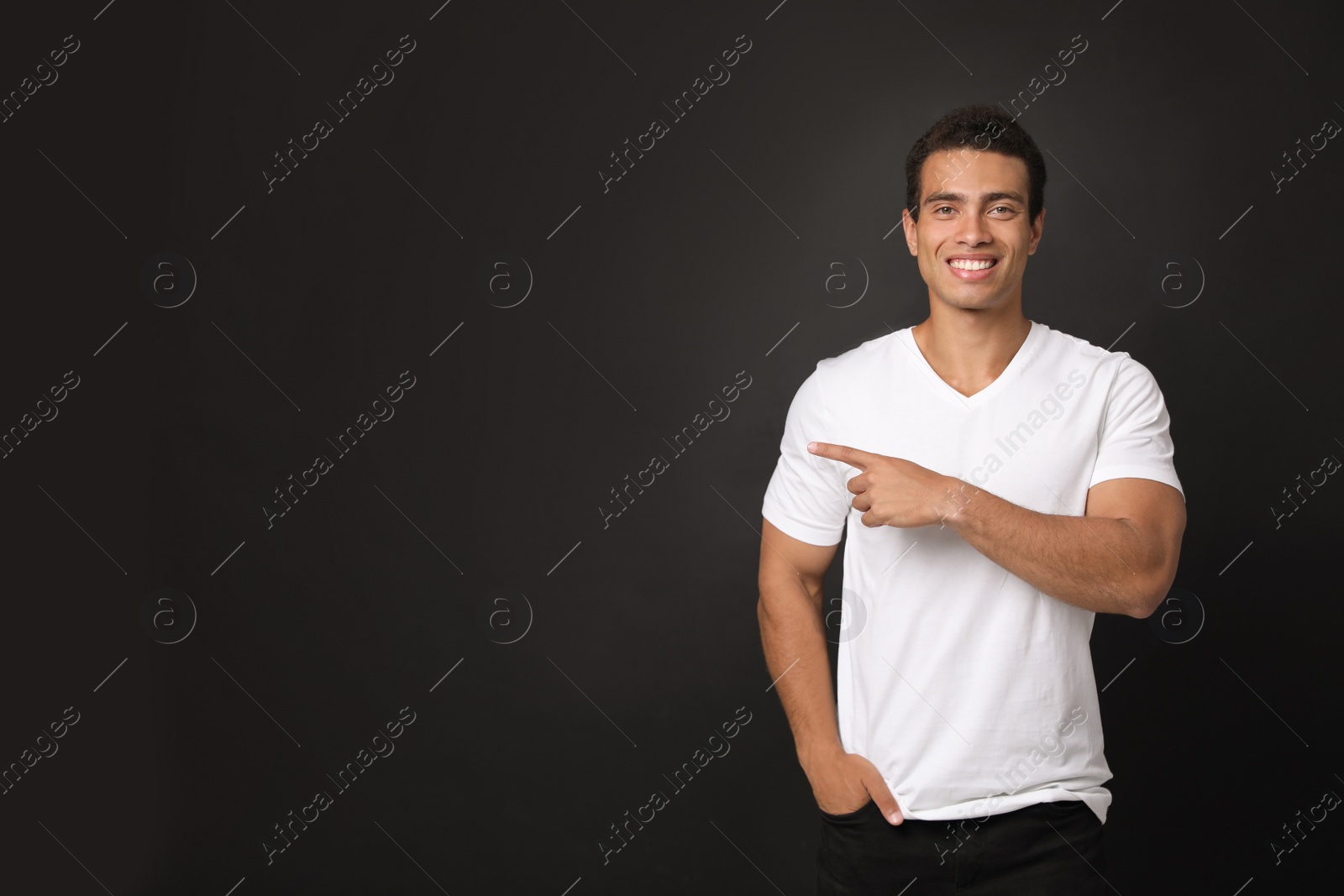 Photo of Handsome young African-American man pointing side on black background. Space for text