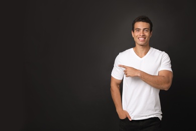 Handsome young African-American man pointing side on black background. Space for text