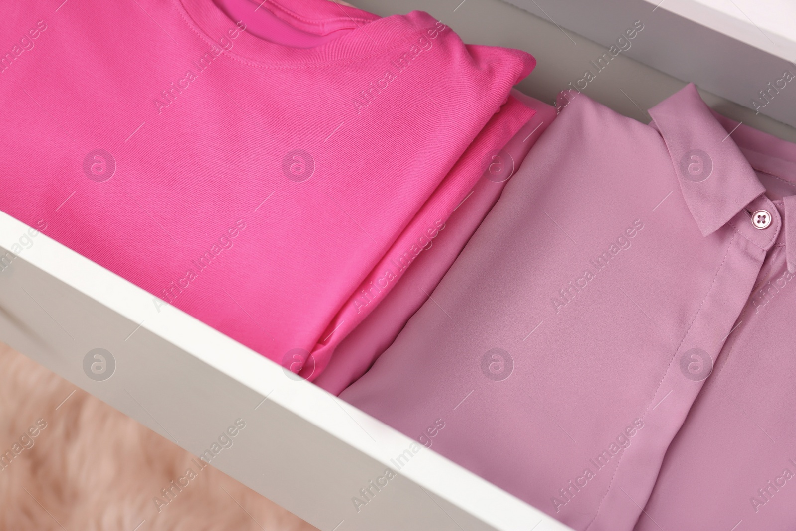 Photo of Folded pink clothes in white chest of drawers indoors, closeup