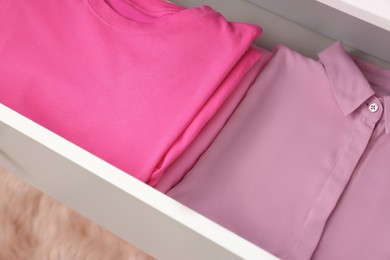 Photo of Folded pink clothes in white chest of drawers indoors, closeup