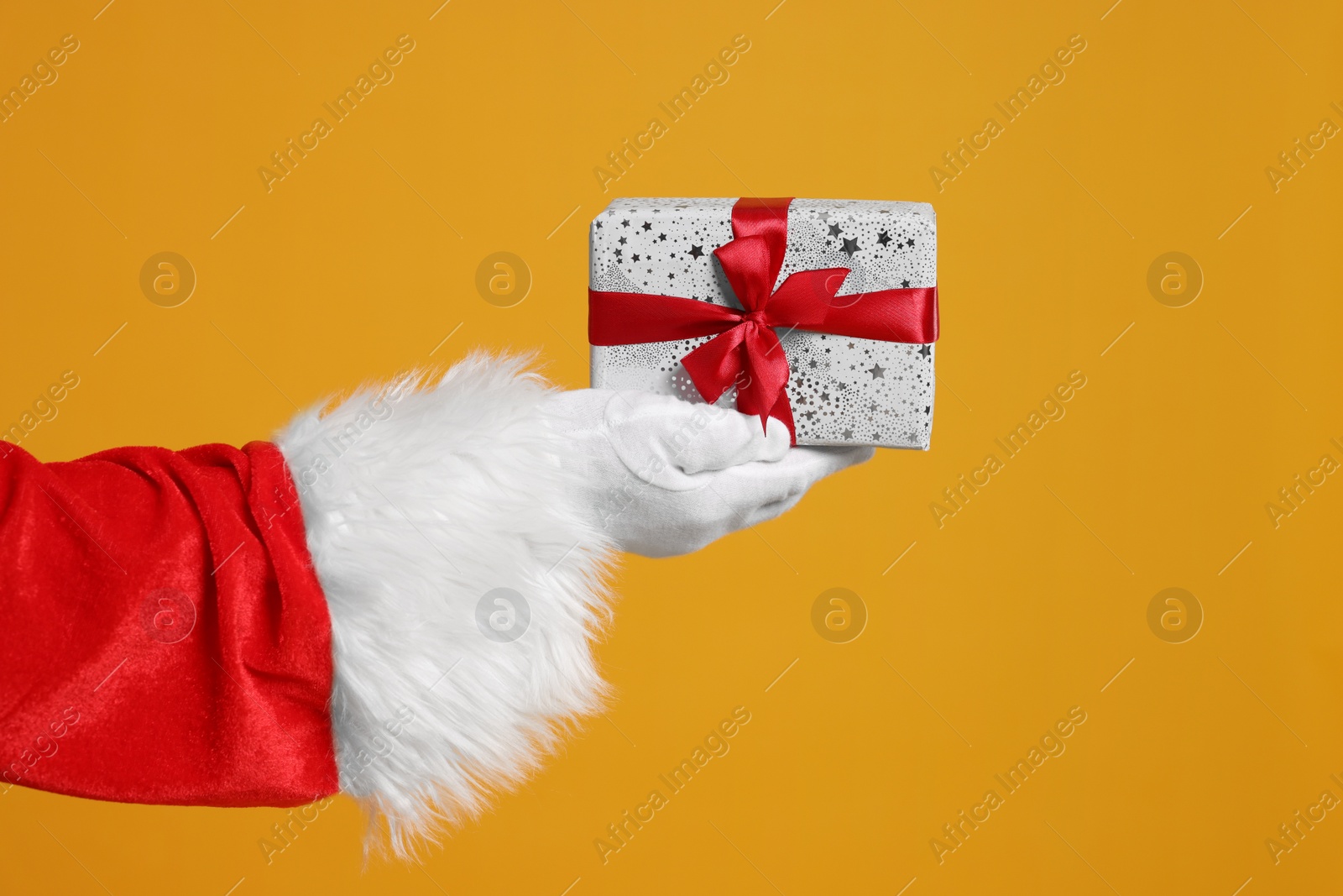 Photo of Santa Claus holding Christmas gift on orange background, closeup