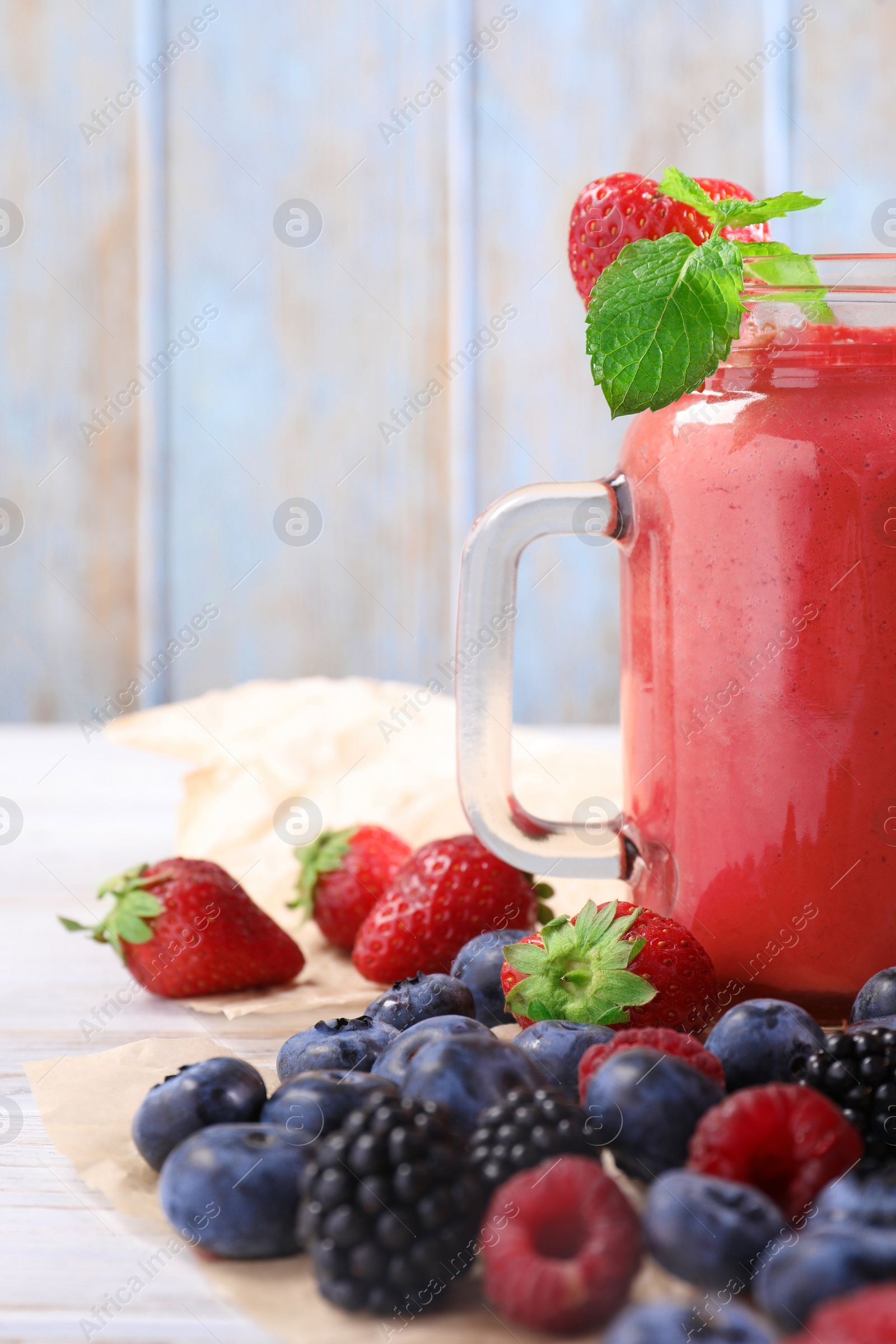 Photo of Mason jar of berry smoothie and fresh ingredients on white wooden table, closeup