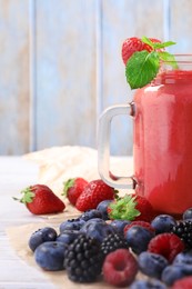 Mason jar of berry smoothie and fresh ingredients on white wooden table, closeup