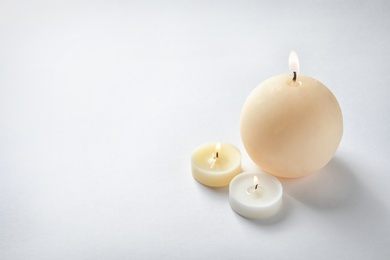 Burning wax candles of different shapes on white background