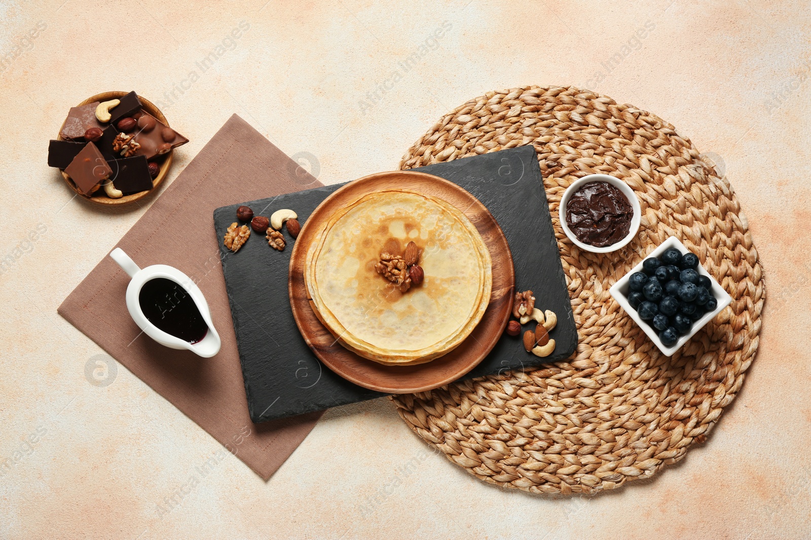 Photo of Delicious crepes with nuts, blueberries, chocolate and jam on beige table, flat lay