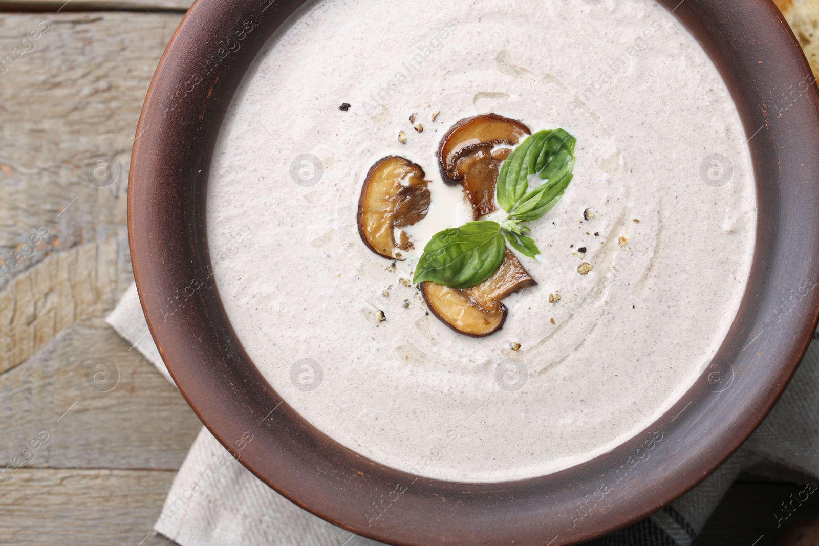 Photo of Delicious homemade mushroom soup in ceramic pot and fresh ingredients on wooden table