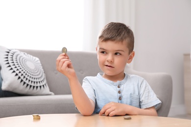 Photo of Cute little boy holding coin at home