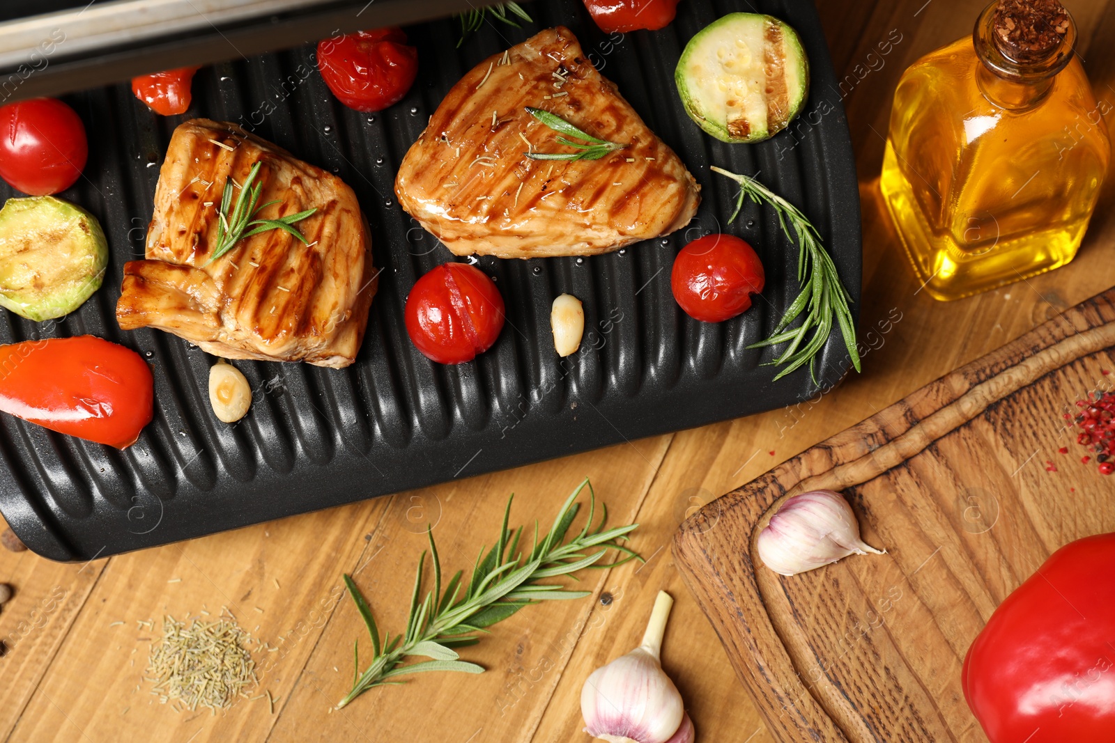 Photo of Electric grill with different products on wooden table, above view