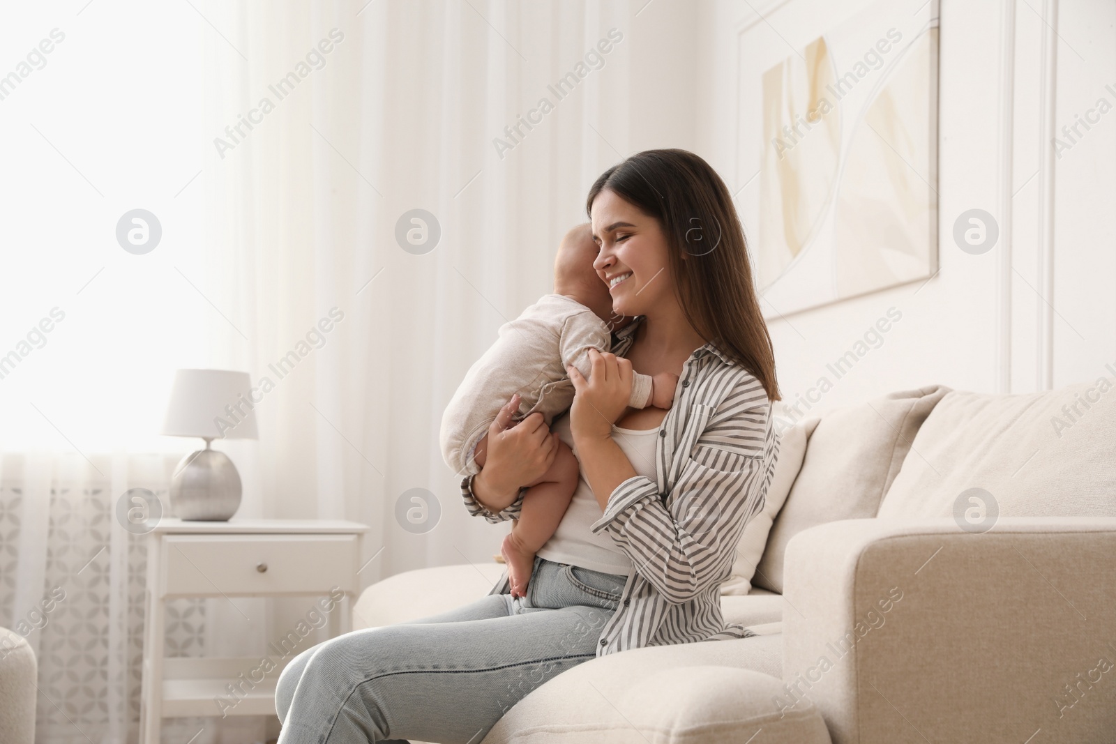 Photo of Young woman with her little baby on sofa at home