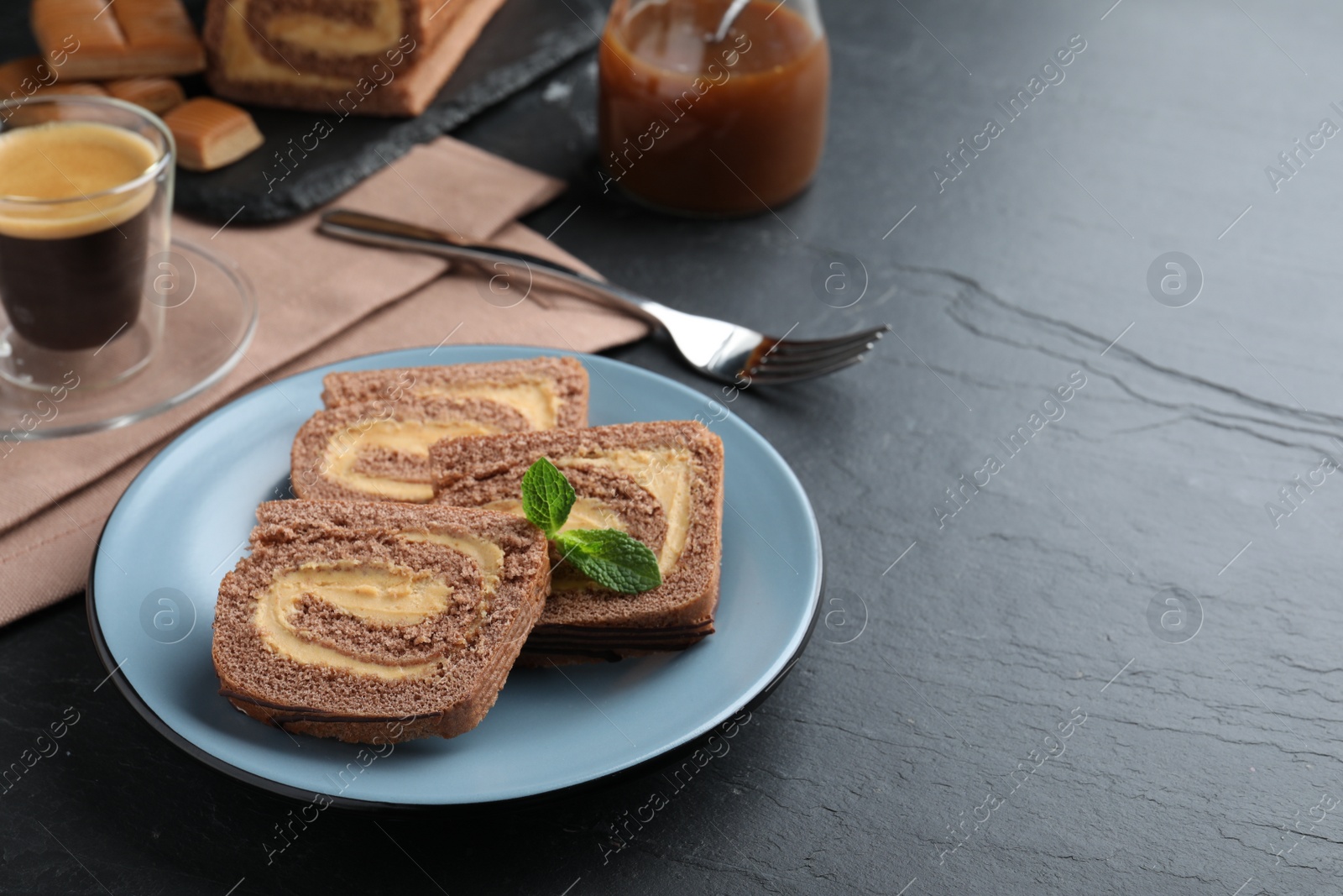 Photo of Tasty chocolate cake roll with cream on black table, space for text