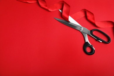 Photo of Stylish scissors and red ribbon on color background, flat lay with space for text. Ceremonial tape cutting