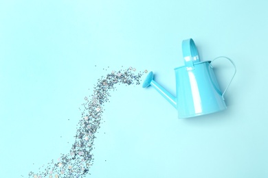 Photo of Watering can with silver glitter confetti imitating water  flow on cyan background, flat lay