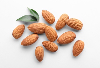 Photo of Organic almond nuts and leaves on white background, top view. Healthy snack