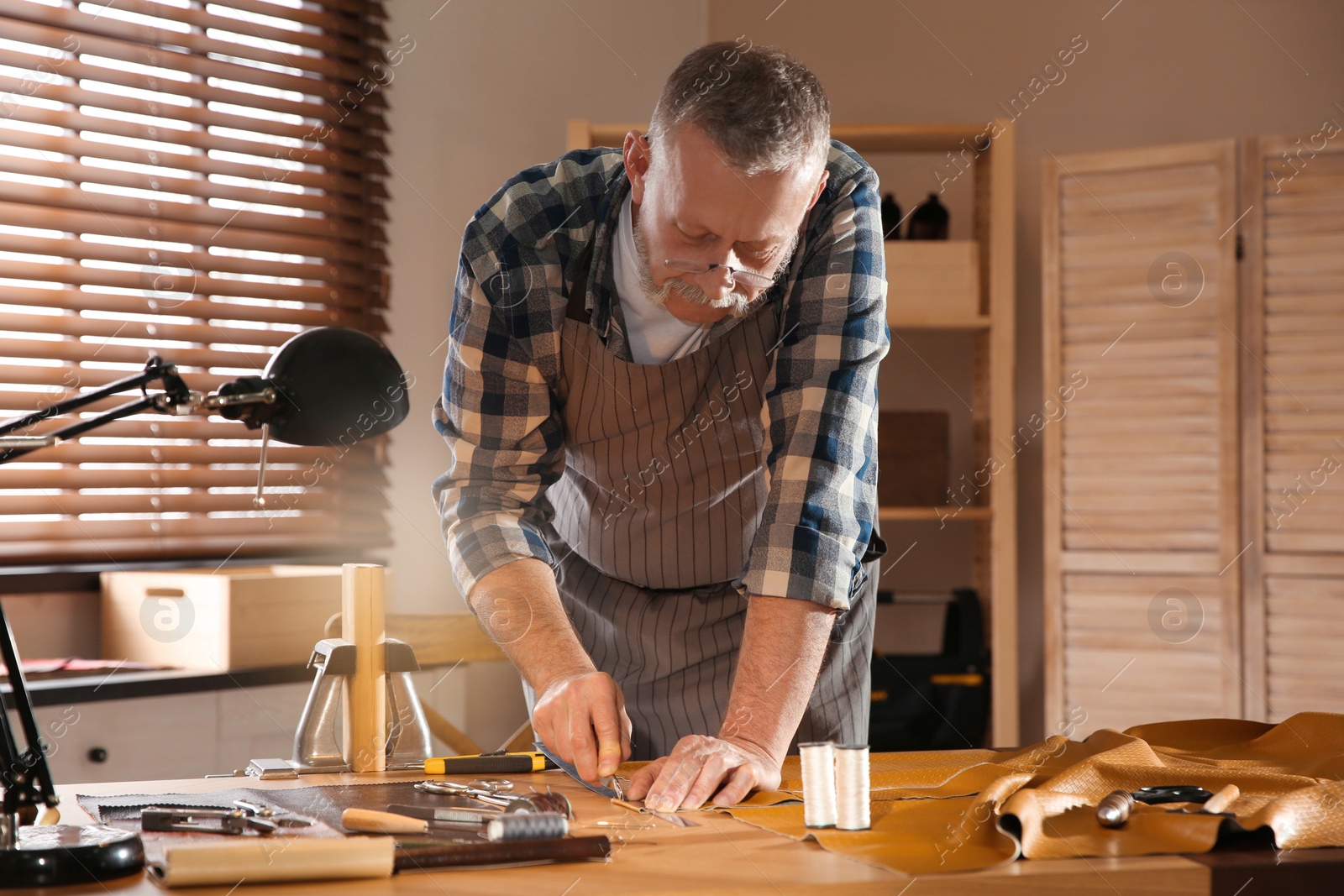 Photo of Man marking leather with roller in workshop