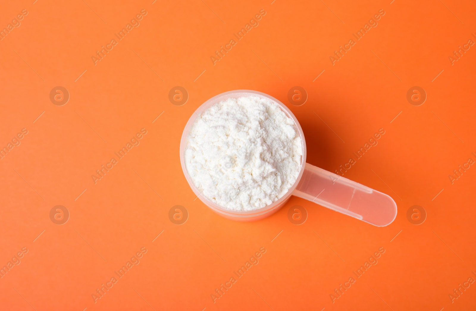 Photo of Scoop of protein powder on orange background, top view