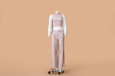 Photo of Female mannequin with bag dressed in stylish crop top and pants on beige background