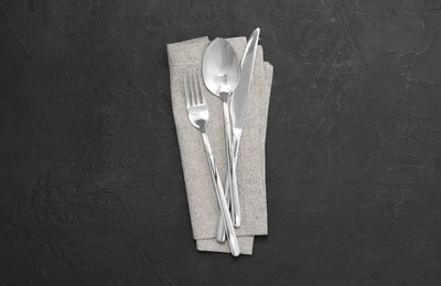 Photo of Beautiful cutlery set and kitchen towel on black table, top view