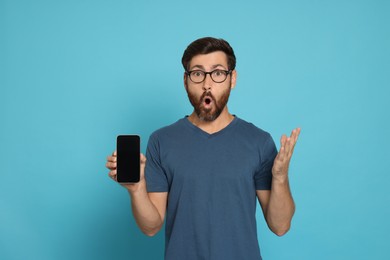 Emotional man with smartphone on light blue background